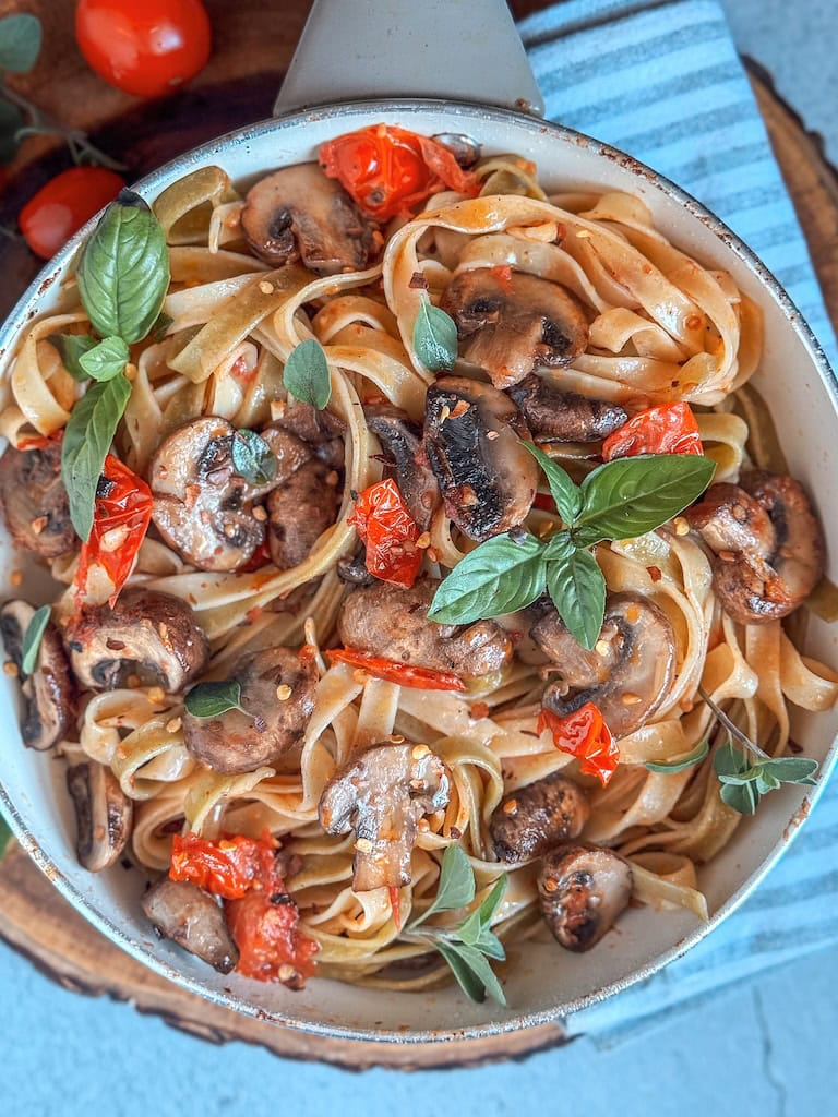 Fork twirling spinach pasta with mushrooms, cherry tomatoes, and basil on a plate.