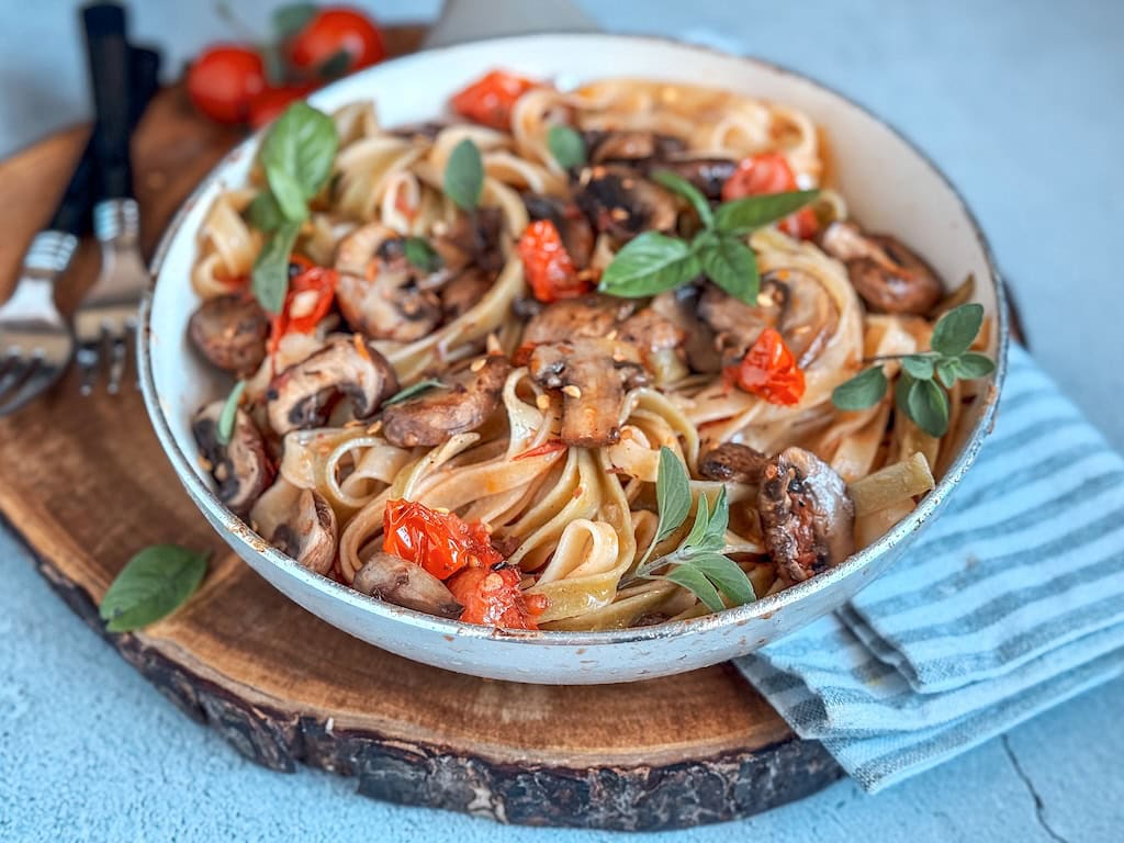 Fork twirling spinach pasta with mushrooms, cherry tomatoes, and basil on a plate.