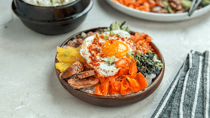 Bibimbap is a colorful Korean rice bowl with vegetables, beef, eggs, and kimchi. Let's learn a bit about tis recipe and how to make this easy, customizable, and healthy meal at home with leftovers or fresh ingredients. Some recipes are made with ingredients. Others—with intention. This one, I believe, is made with love.