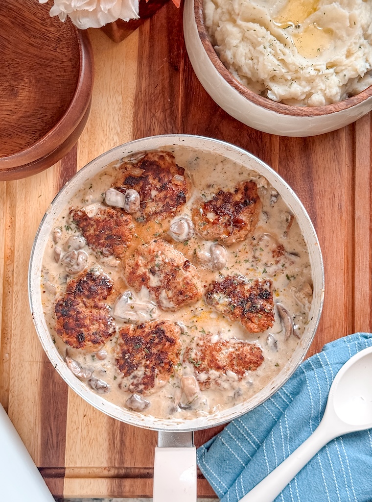 Golden brown turkey patties simmering in creamy mushroom sauce with sliced mushrooms