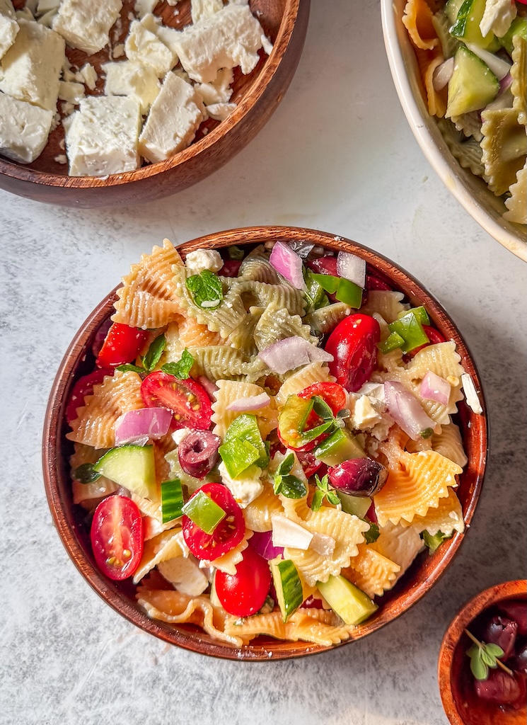 Overhead view of homemade Greek-inspired pasta salad with Mediterranean vegetables and lemon oregano dressing.