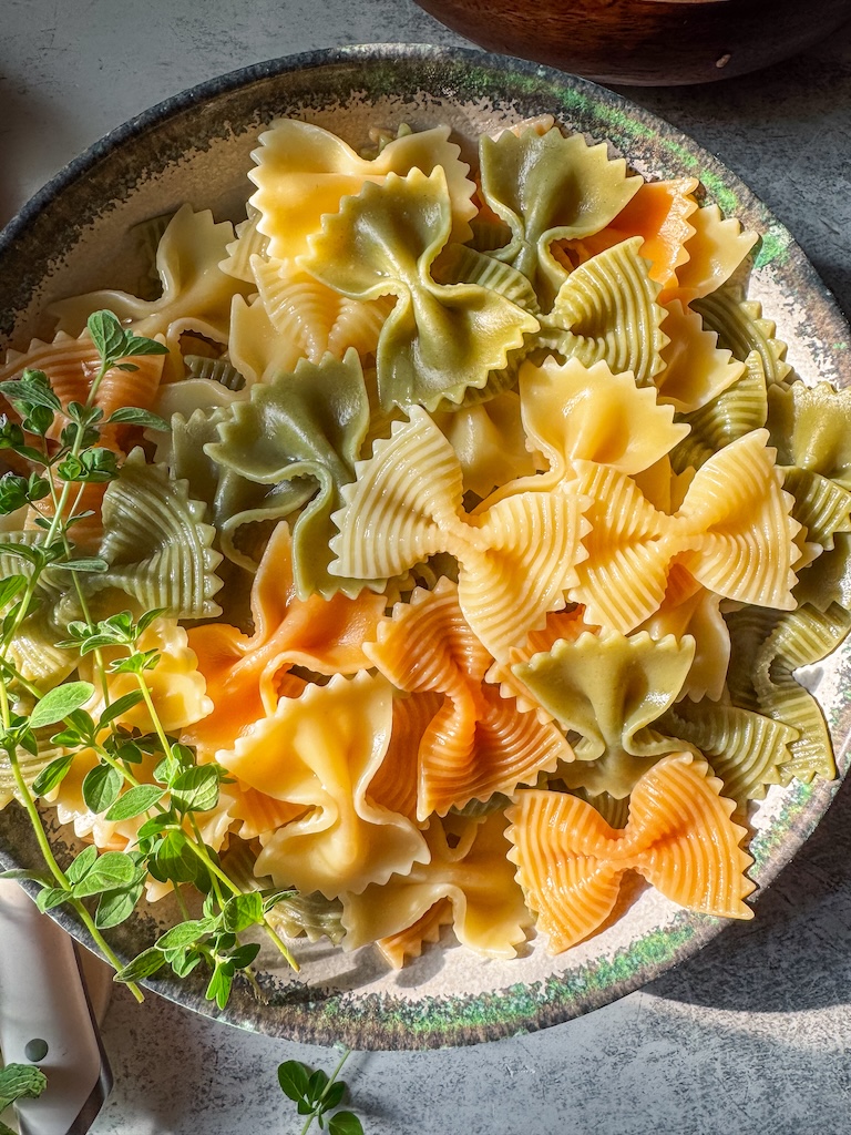 Greek-inspired pasta salad with feta cheese, Kalamata olives, fresh vegetables, and herbs in a wooden serving bowl.
