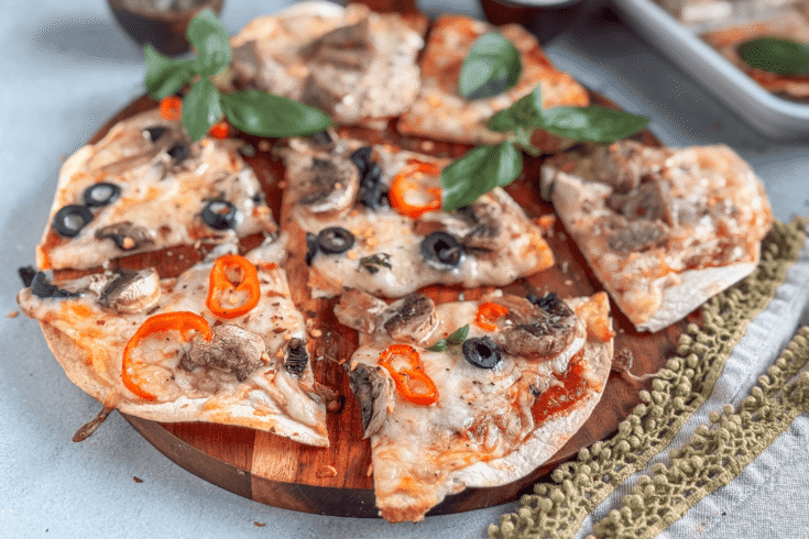 Crispy tortilla pizzas topped with cheese, peppers, and olives on a rustic board.