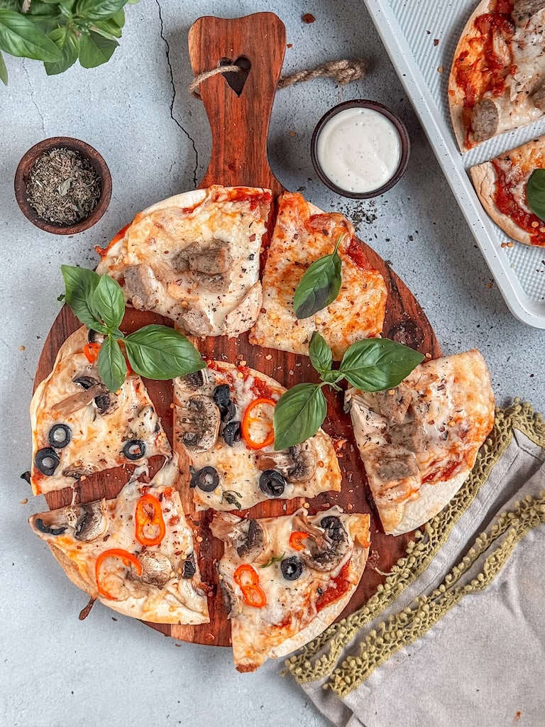 Crispy tortilla pizzas topped with cheese, peppers, and olives on a rustic board.