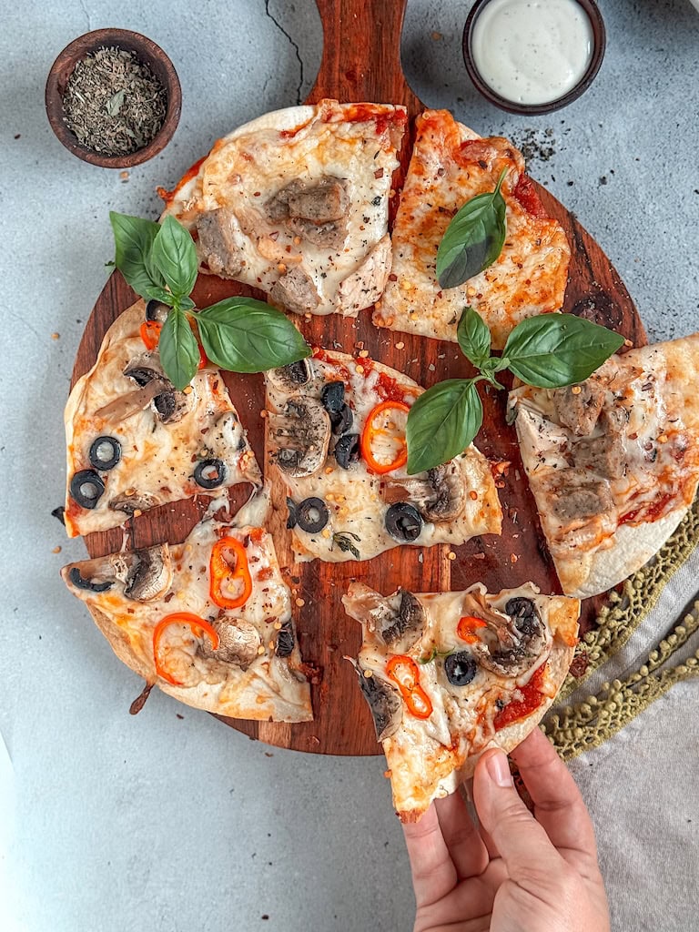 Crispy tortilla pizzas topped with cheese, peppers, and olives on a rustic board.