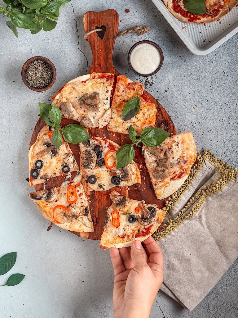 Crispy tortilla pizzas topped with cheese, peppers, and olives on a rustic board.