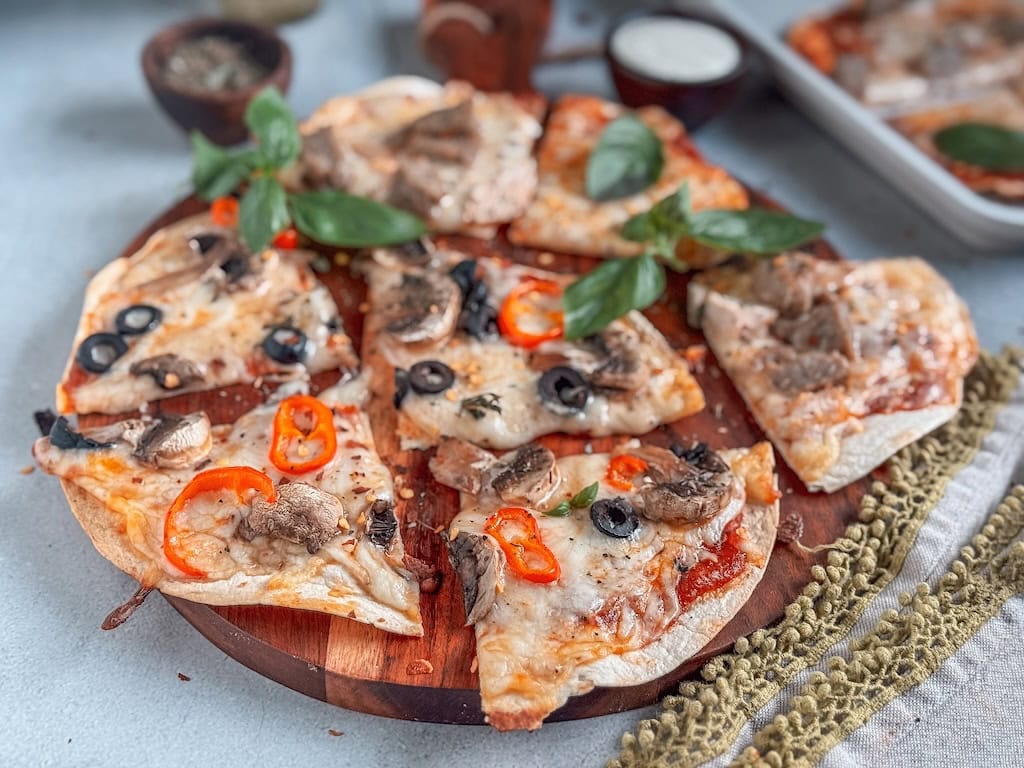 Crispy tortilla pizzas topped with cheese, peppers, and olives on a rustic board.