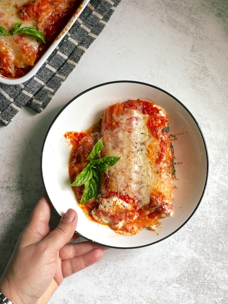 Spinach and ricotta stuffed pasta bake with marinara sauce, melted mozzarella cheese, and fresh basil baked until bubbly and golden in a white baking dish.