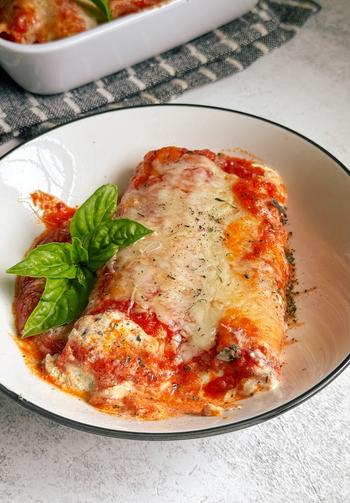 Spinach and ricotta stuffed pasta bake with marinara sauce, melted mozzarella cheese, and fresh basil baked until bubbly and golden in a white baking dish.