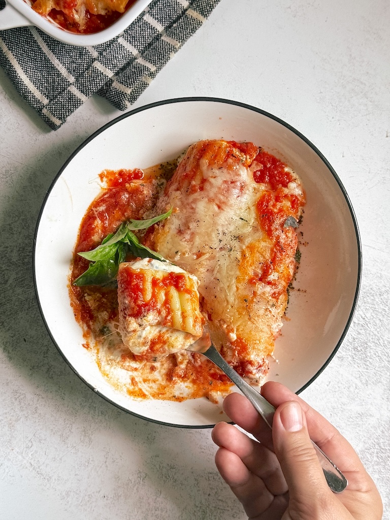 Spinach and ricotta stuffed pasta bake with marinara sauce, melted mozzarella cheese, and fresh basil baked until bubbly and golden in a white baking dish.