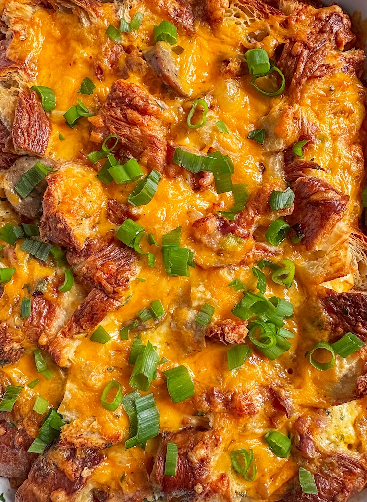 Golden cheesy croissant breakfast casserole topped with fresh scallions