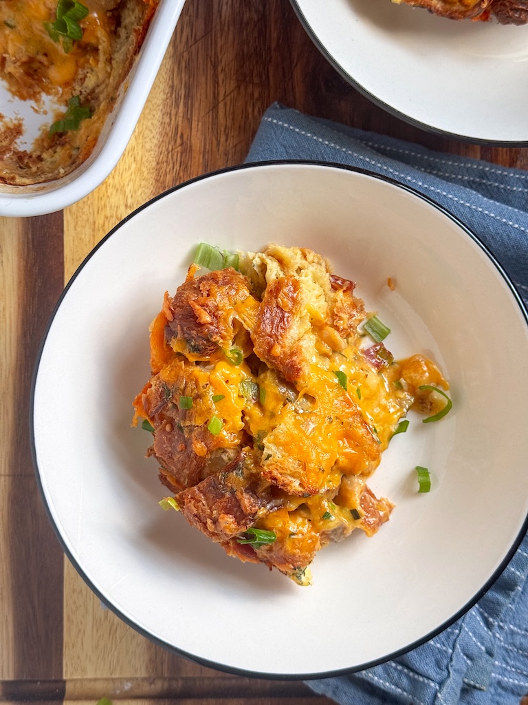 Golden cheesy croissant breakfast casserole topped with fresh scallions