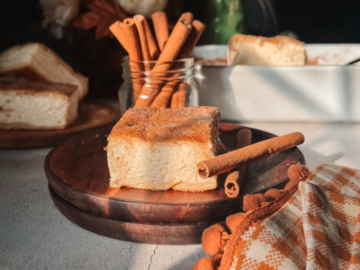 Churro cheesecake bar with thick vanilla cheesecake filling and cinnamon-sugar crescent pastry.
