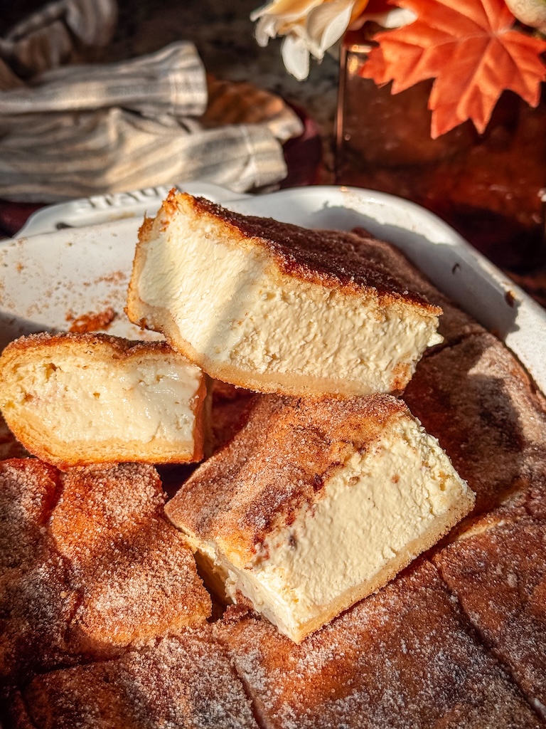 Churro cheesecake bar with thick vanilla cheesecake filling and cinnamon-sugar crescent pastry.